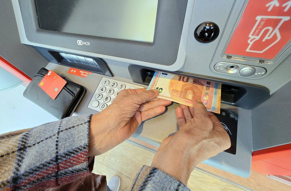 Cliente de banco sacando dinero (billetes) de un cajero automático en una calle de Vigo.
