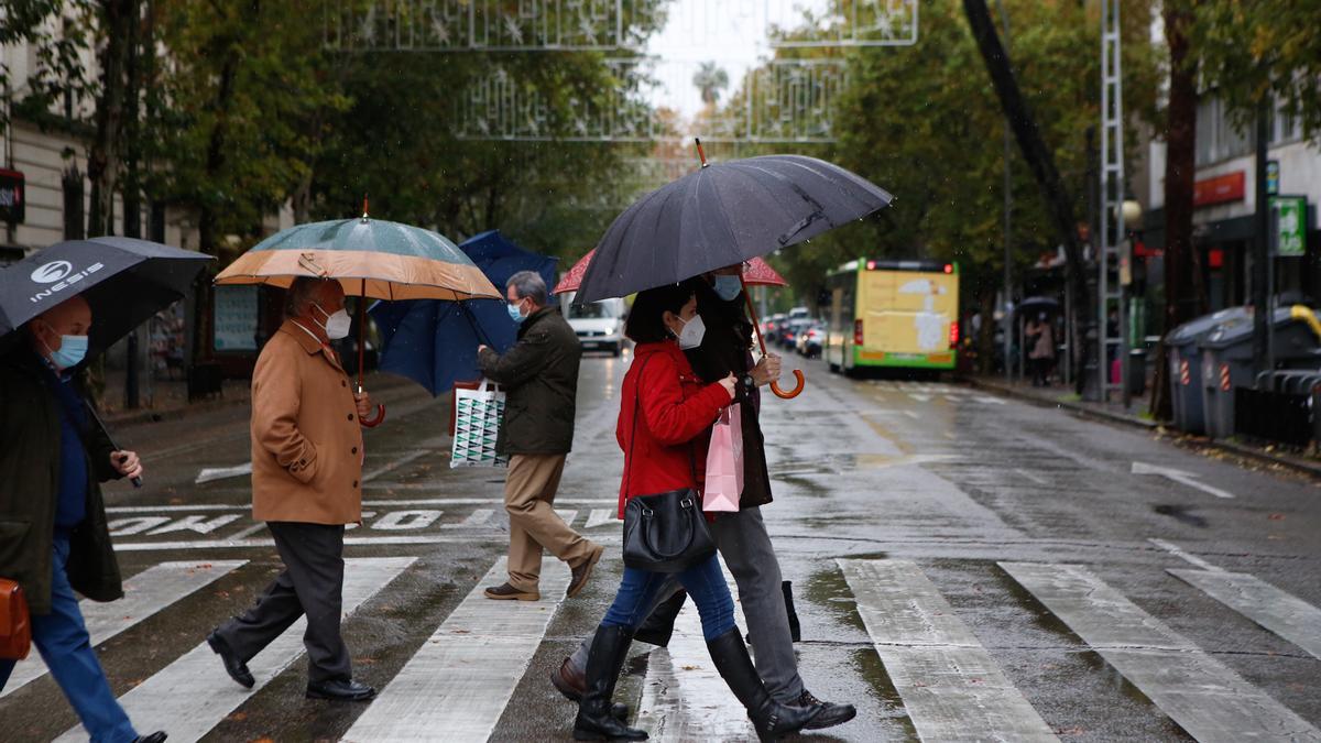 Varios peatones cruzan una calle con el paraguas en la mano.