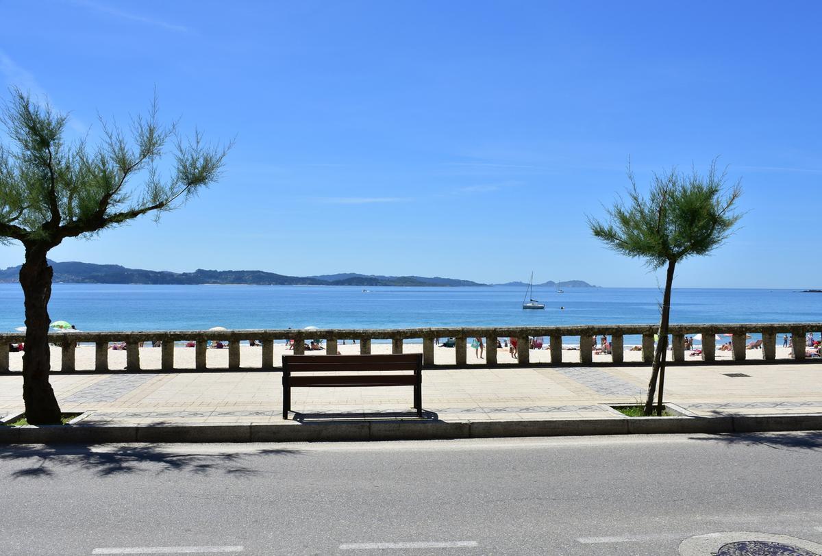 Vista de la playa de Silgar desde el paseo marítimo con pasamanos de piedra y banco de madera
