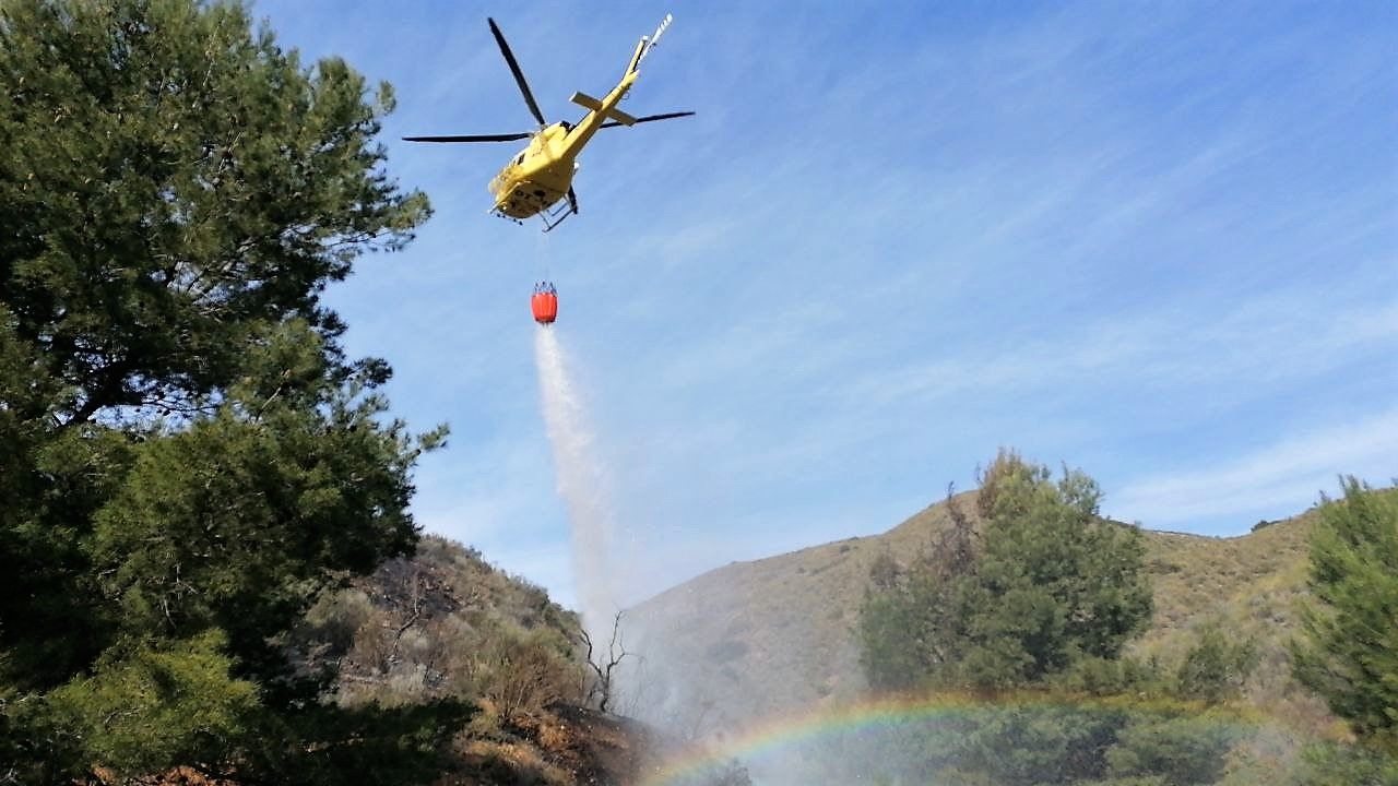 Un arcoíris sale mientras un helicóptero tira agua para apagar el fuego.