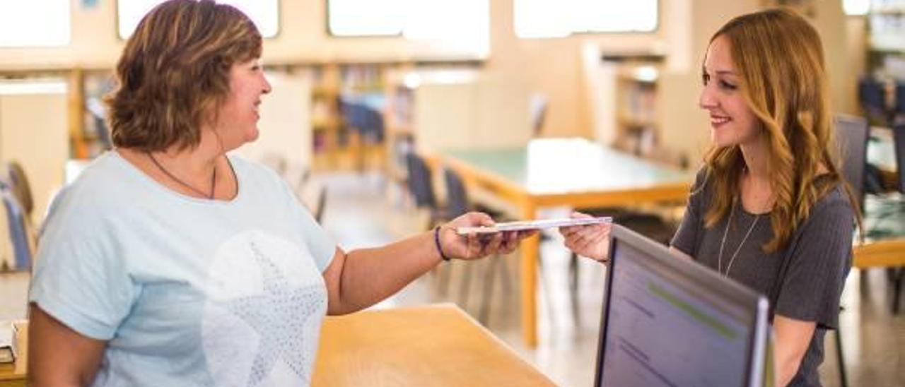 Una vecina de Cullera recoge un libro de la biblioteca municipal.