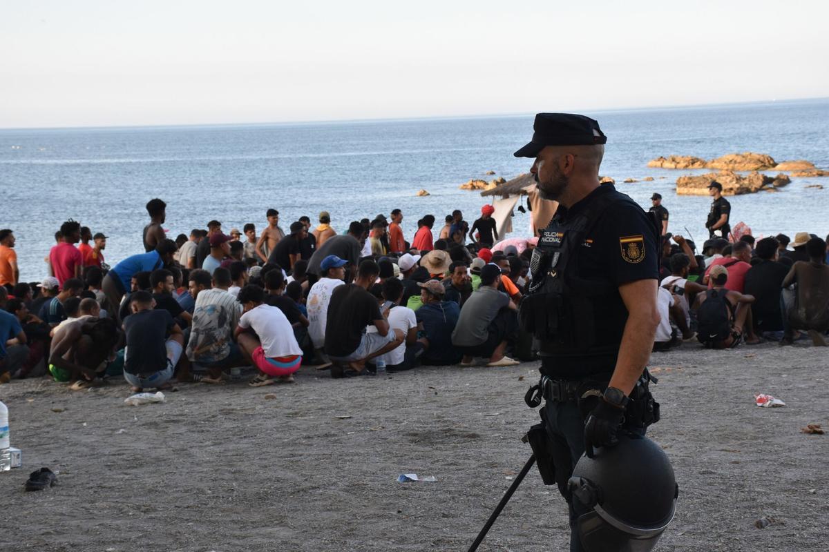 Un policía nacional, junto a decenas de migrantes, el pasado fin de semana en una playa de Ceuta.