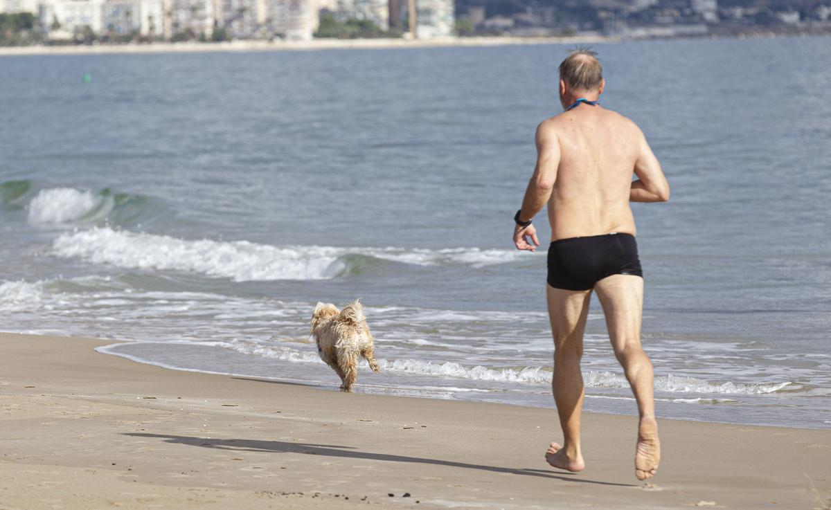 Un hombre corriendo con su perro por la orilla de la Playa de San Juan.