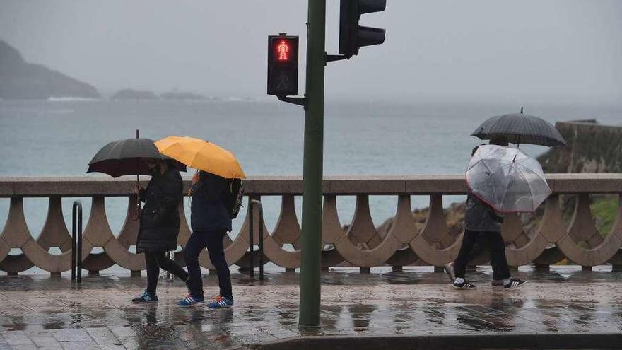 Gente protegiéndose de la lluvia en el paseo marítimo de A Coruña.