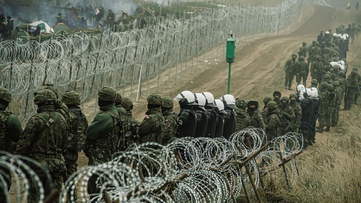 Soldats i policies polonesos observen els immigrants a la frontera amb Bielorússia. | IREK DOROZANSKI/REUTERS