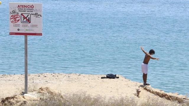 Un menor a punt de saltar des de les roques del Miracle a Tarragona, davant d’un cartell de prohibició.