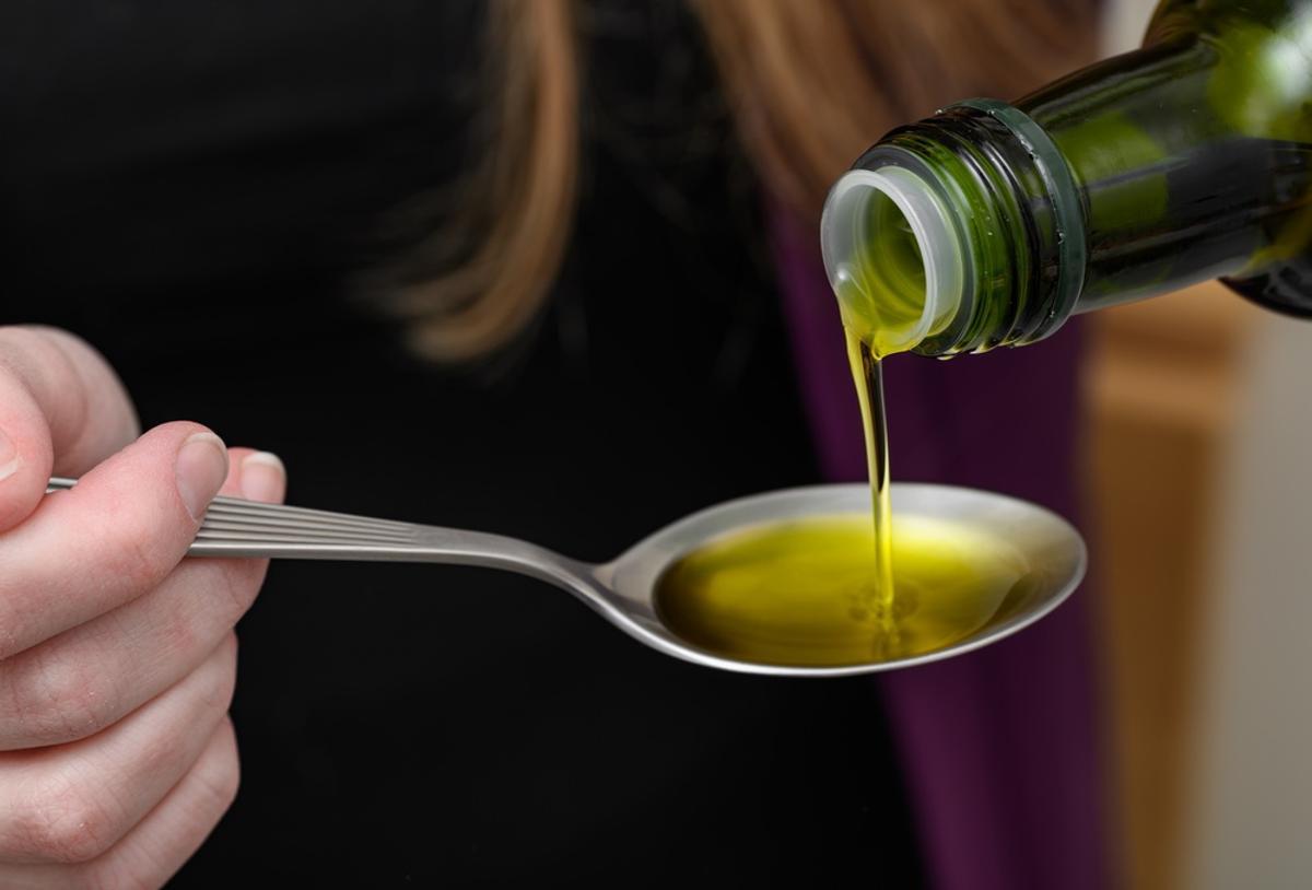 Una mujer vierte aceite de oliva extra virgen en una cuchara mientras elabora una receta.