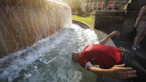 Un hombre se refresca en una fuente en Barcelona