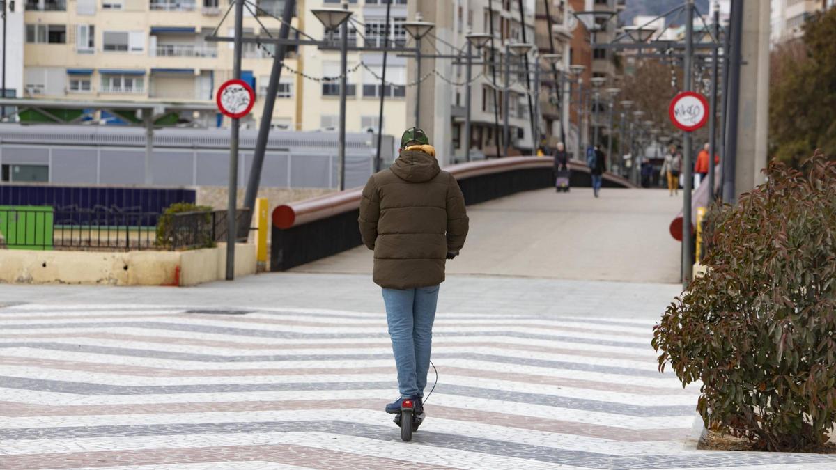 Un hombre circula con patinete eléctrico por la pasarela del paseo de les Germanies de Gandia