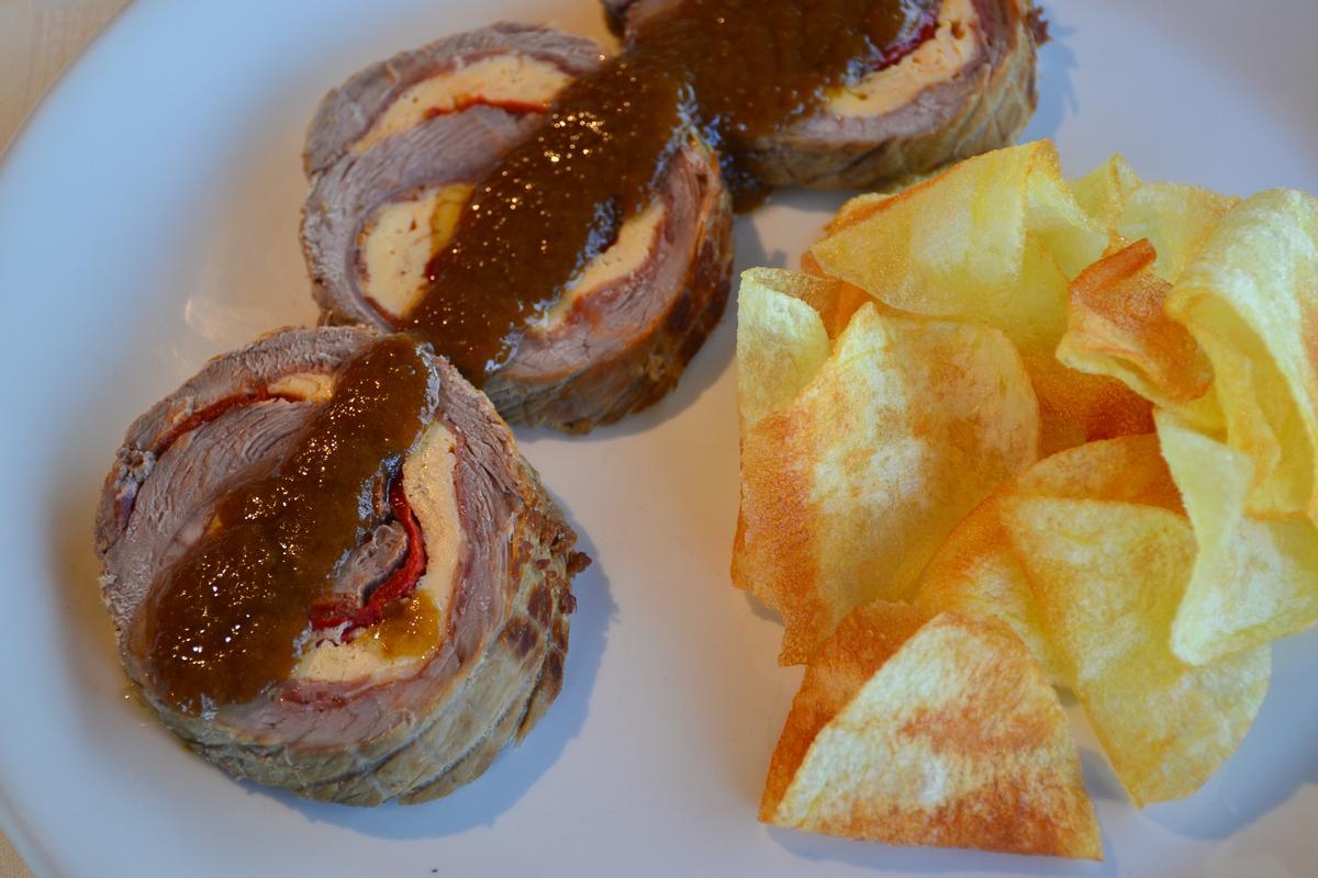 Rollo de carne guisado y relleno, acompañado de patatas chips caseras.