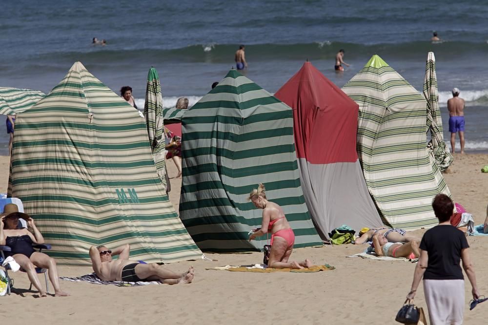 Gijoneses y visitantes se lanzan a la playa en una jornada calurosa.