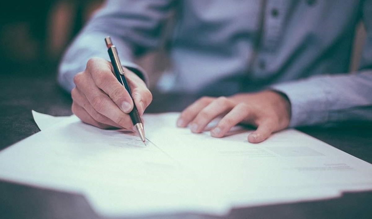 Un hombre en el momento de firmar un documento ante notario.