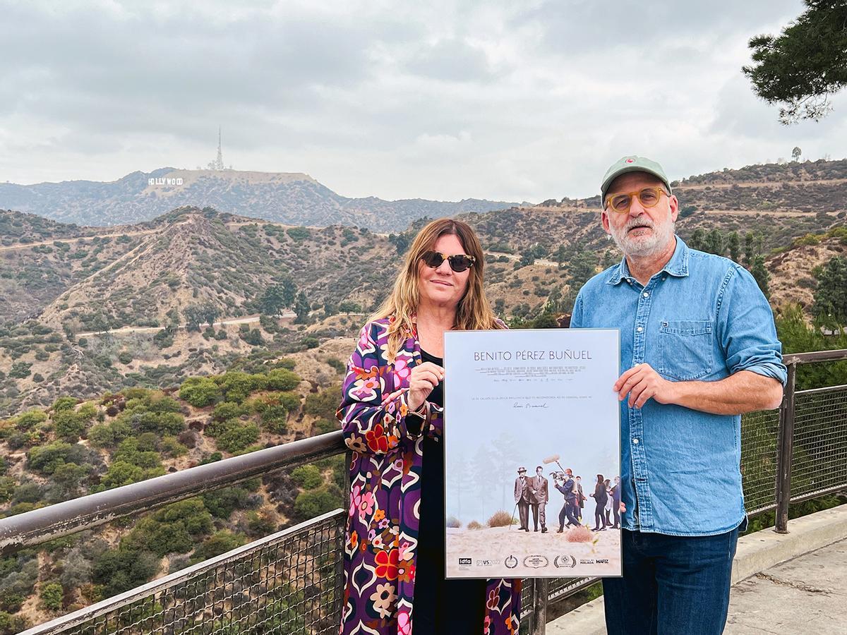 La productora Marta de Santa Ana y el director Luis Roca sostienen el cartel de su película ‘Benito Pérez Buñuel’ en el Observatorio Griffith, con la vista de Hollywood al fondo.