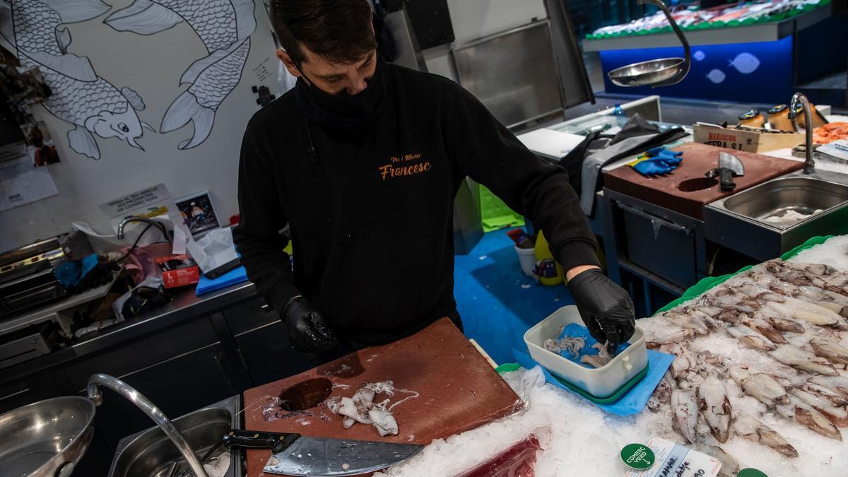 Un pescadero coloca unos calamares en un táper de un clienta en el mercado del Ninot de Barcelona.