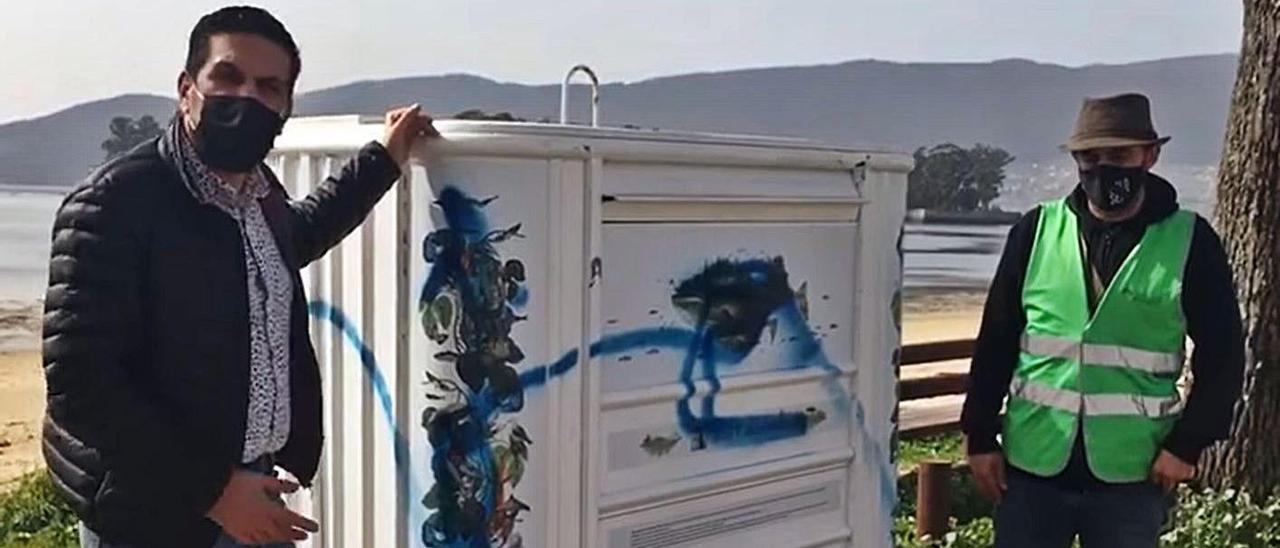 El edil de Cultura de Redondela, Daniel Boullosa (izq.), y el de Medio Ambiente, Roberto Villar, muestran las pintadas vandálicas realizadas con “spray” en uno de los contenedores de la playa de Cesantes. |