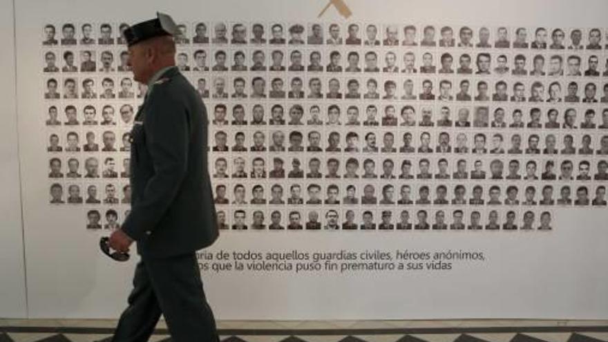 Un guardia civil pasa delante de la imagen con los 243 agentes asesinados; a la derecha, dos detalles de la muestra, uno referido al atentado de Mutxamel.