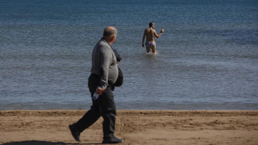 Un hombre pasea mientras uno se baña en la playa de La Malvarrosa, en imagen de archivo