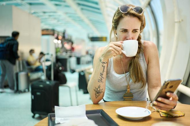Mujer tomando café y usando el teléfono esperando en la sala del aeropuerto