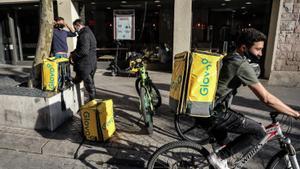 Repartidores de Glovo esperan su pedido a las puertas de una cadena de restaurantes de comida rápida.