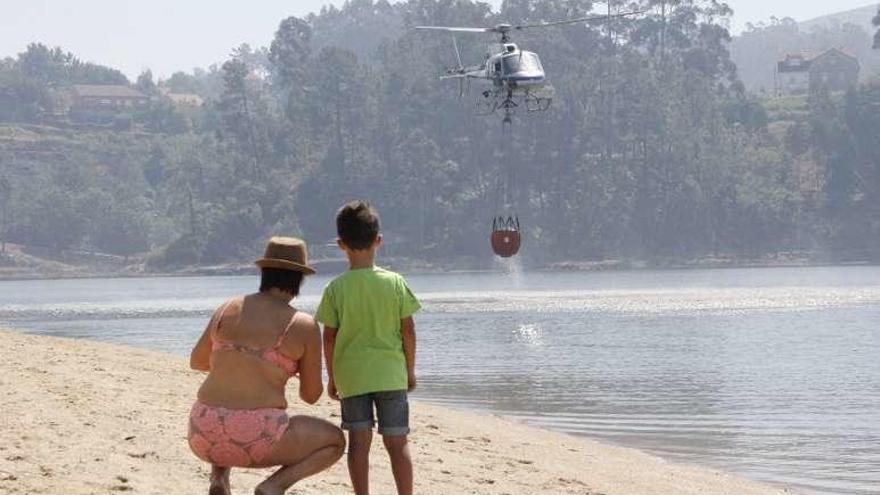 Una mujer y un niño observan a un helicóptero repostar agua. // S.A.