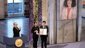 La líder del Comité Nobel, Berit Reiss-Andersen, aplaude mientras Kiana Rahmani y Ali Rahmani posan con el premio en nombre de su madre durante la ceremonia del Premio Nobel de la Paz 2023