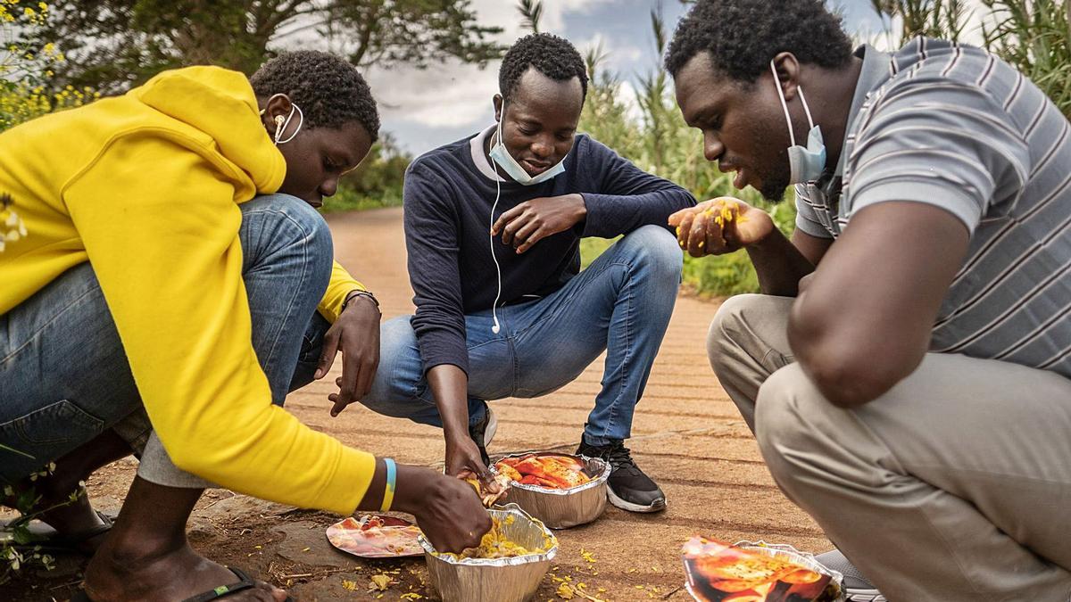 Migrantes comiendo arroz ofrecido por una empresa solidaria en el exterior del campamento de Las Raíces.