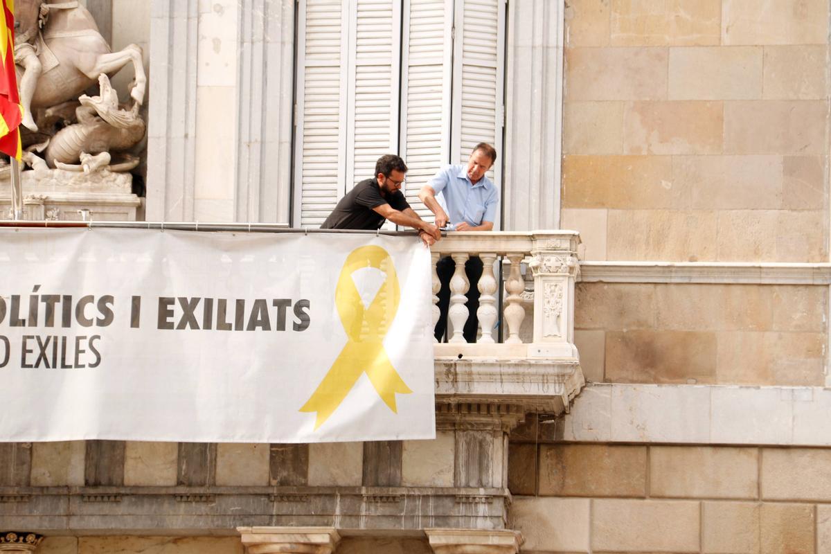 Dos treballadors comencen a treure la pancarta dels presos del Palau de la Generalitat