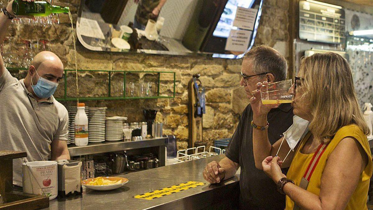 Alberto Rodríguez sirve sidra a dos clientes, ayer, en el restaurante El Ferroviario de la calle Gascona de Oviedo.