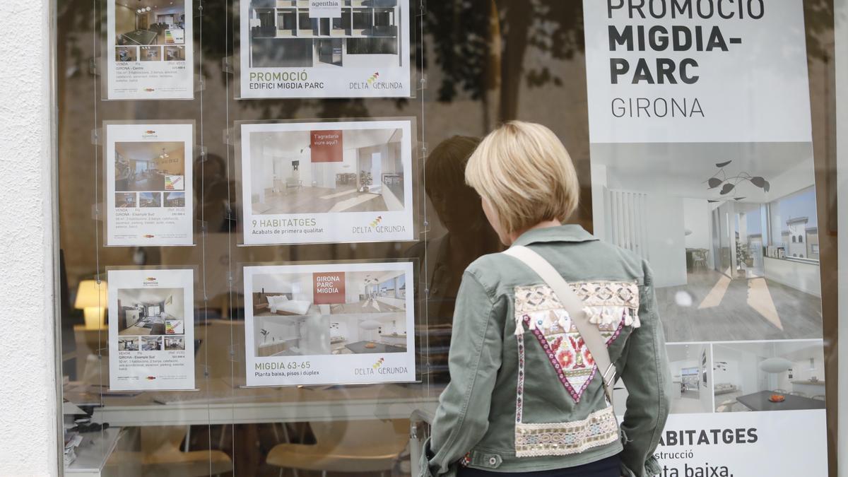 Una dona mira l’aparador d’una immobiliària a Girona.