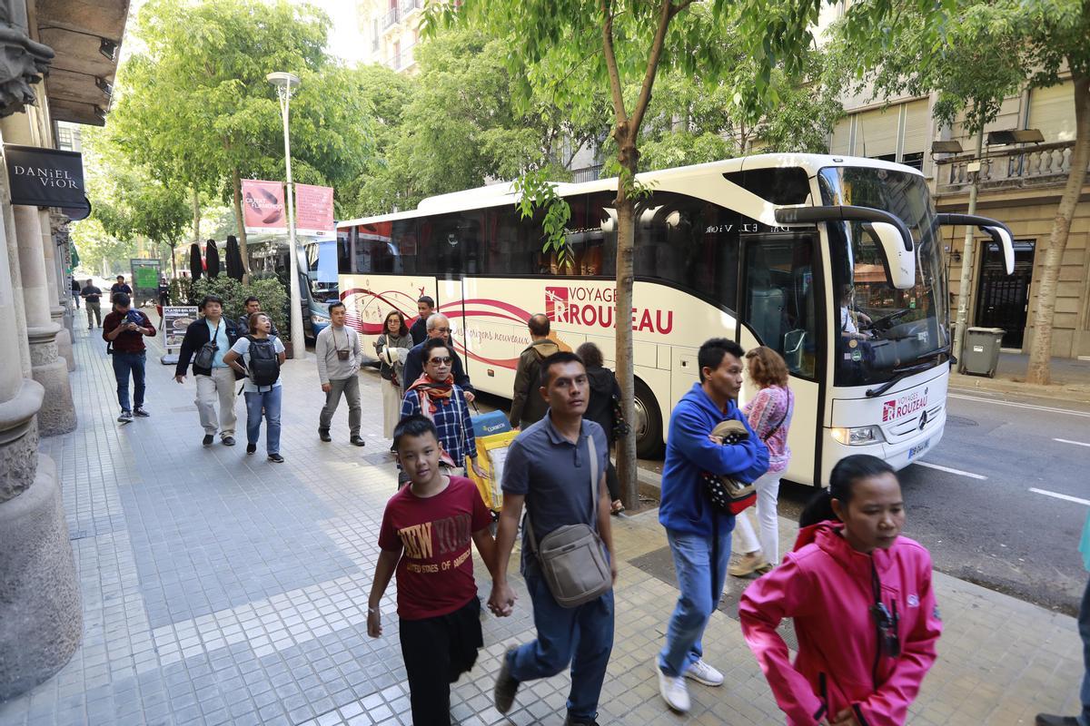 Un grupo de turistas desciende de un autocar turístico, en el Eixample