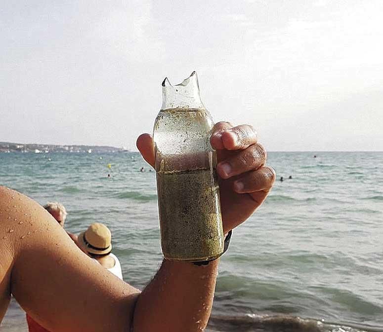 El activista vecinal Xevi Molas enseña a cámara la botella de cristal rota que encontró hace pocos días en el agua de la playa del Arenal.