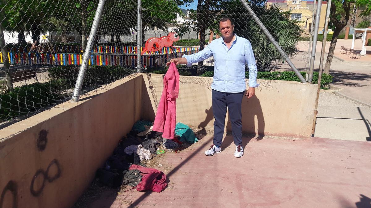 El edil popular muestra alguna de las prendas amontonadas en una esquina de la pista deportiva del parque del barrio.