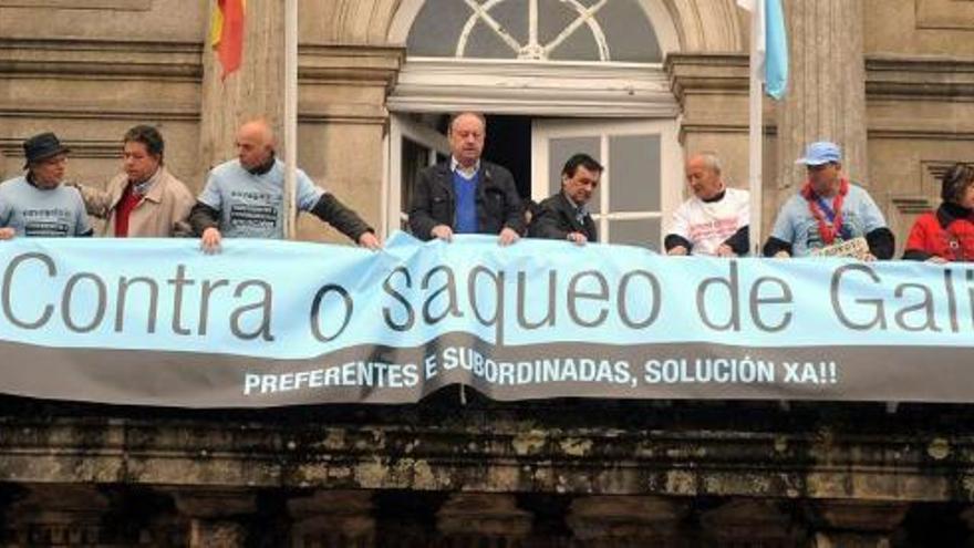 Momento en el que miembros del gobierno local y afectados por las preferentes cuelgan la pancarta del balcón del consistorio.  // R. Vázquez