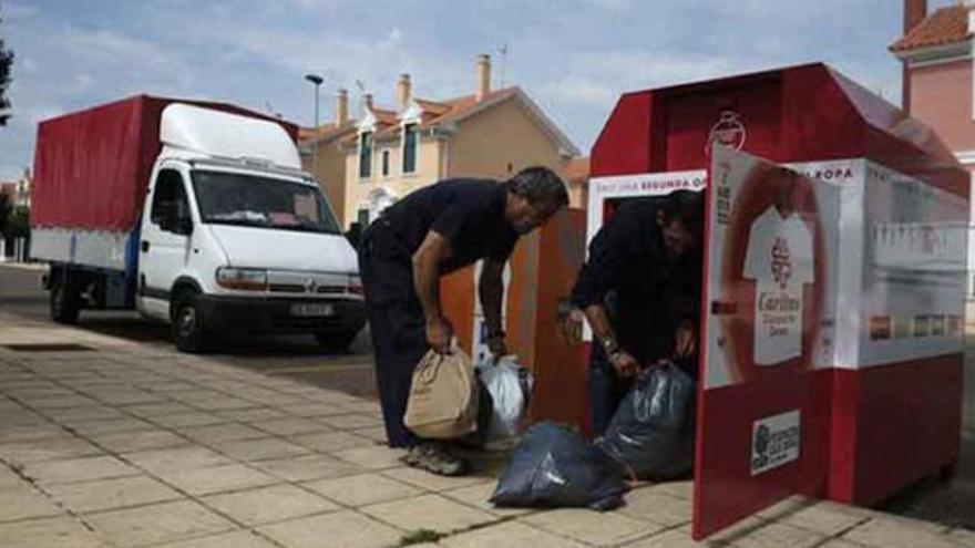 Dos trabajadores recogen la ropa en uno de los contenedores situados en el barrio Siglo XXI.