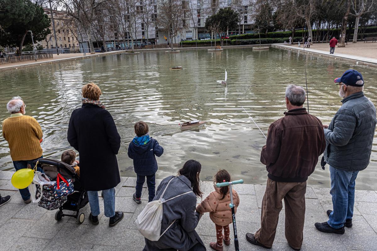 Niños y mayores hacen navegar unos barcos de juguete en el lago de los Jardines del Baix Guinardó.