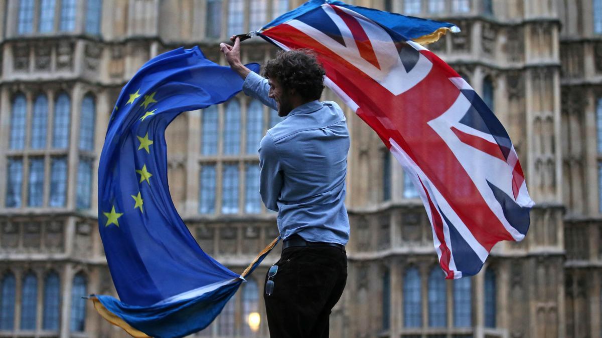 Un joven ondea las banderas británica y europea frente al Parlamento del Reino Unido.