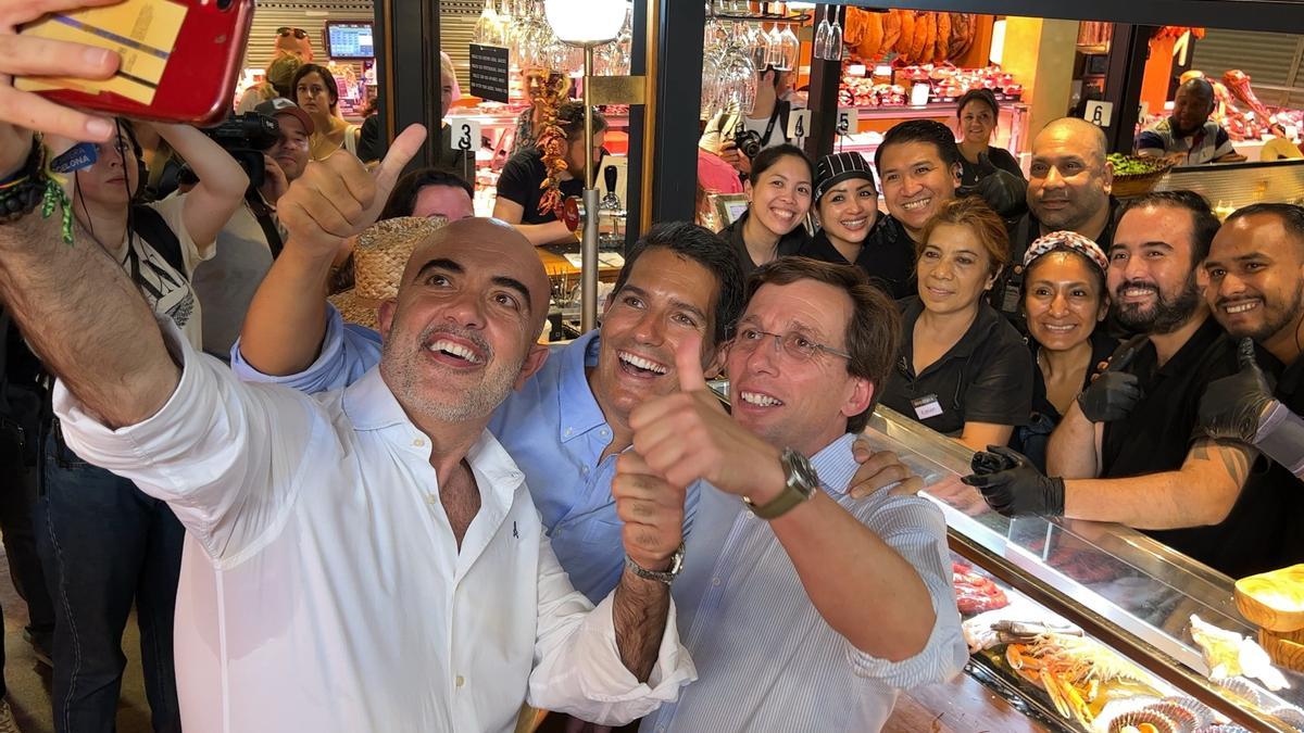 Daniel Sirera, Nacho Martín Blanco i José Luis Martínez-Almeida es fan una foto amb treballadors d'un bar al mercat de la Boqueria de Barcelona.