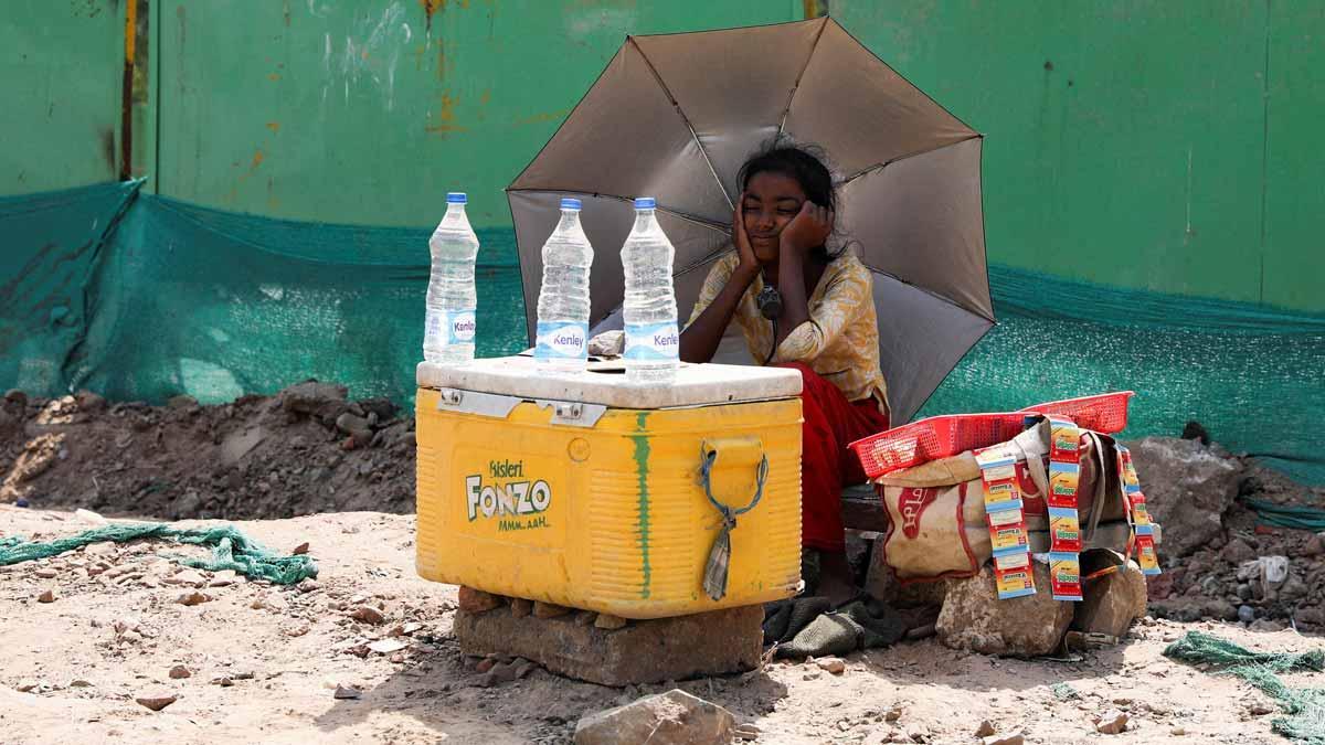 Una chica vende agua en una calle de Nueva Delhi protegida del sol con un paraguas.