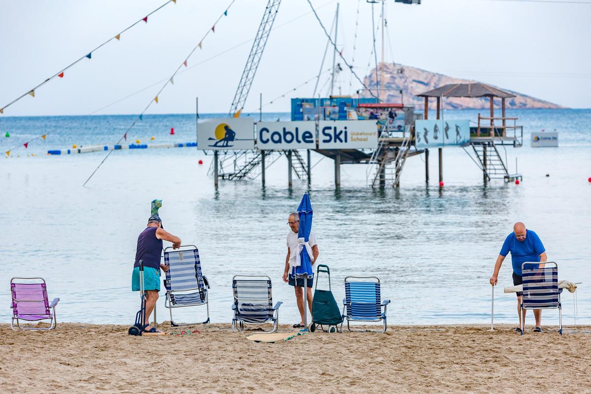 Bañista colocan sombrillas y sillas en la playa de Benidorm.