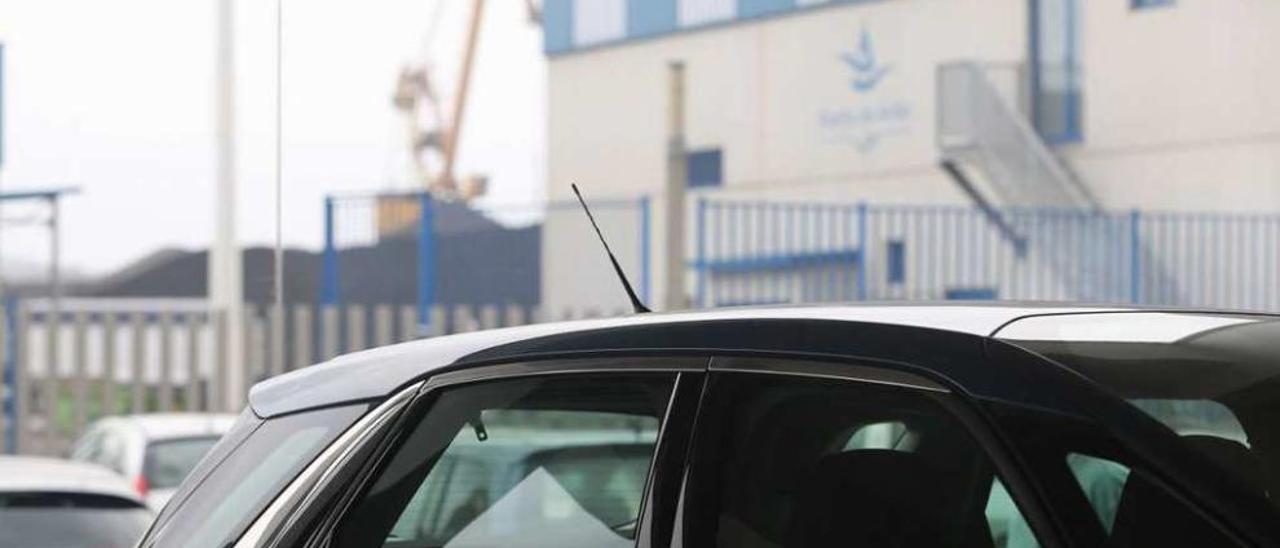 Una pila de carbón asoma al fondo, en el muelle de Raíces, vista desde el interior de un concesionario de automóviles de Las Arobias, una de las empresas que sufren las molestias derivadas del polvo carbonífero.