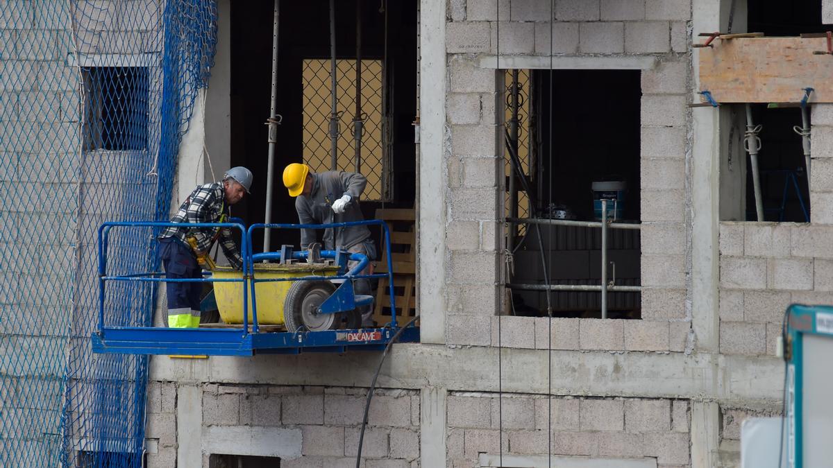 Dos obreros trabajan desde el andamio en la fachada de un edificio en construcción.