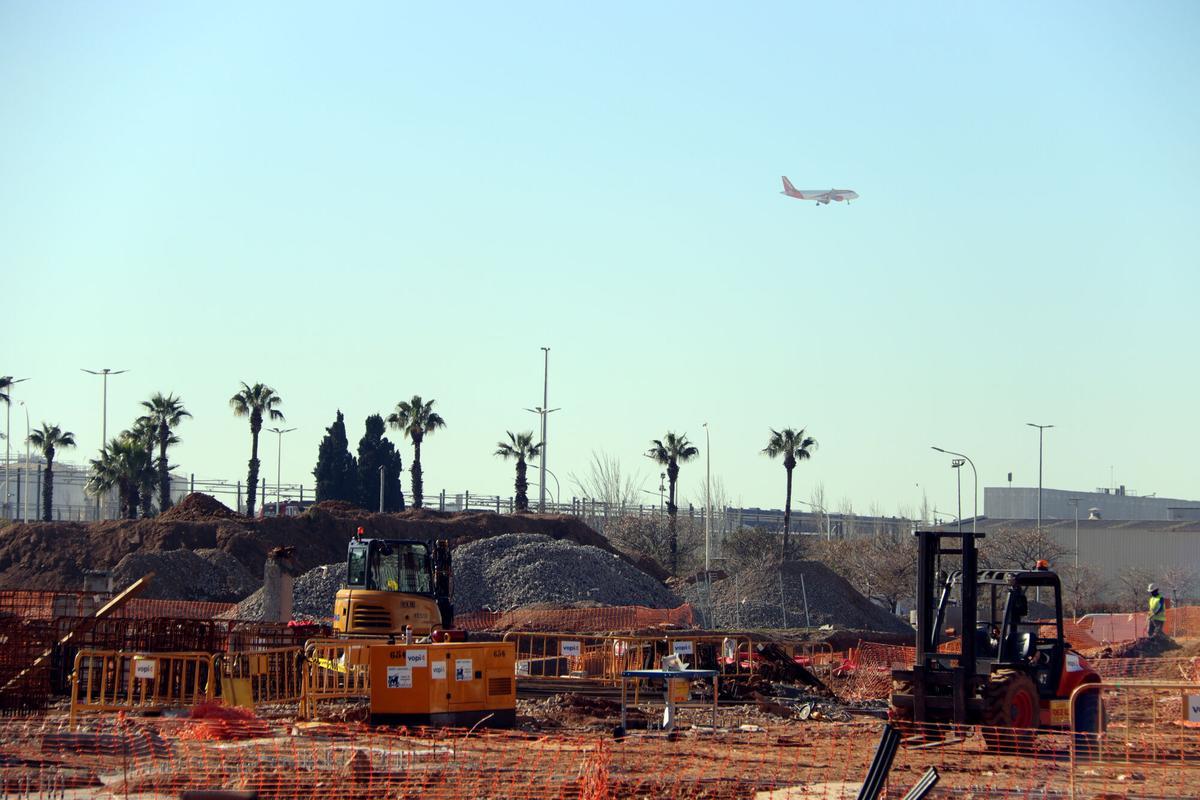 Les obres d'ampliació del DFactory Barcelona a la Zona Franca amb un avió al fons a punt d'aterrar a l'aeroport