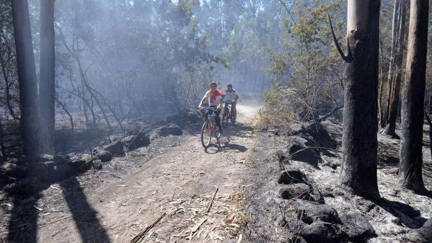 Dos jóvenes pasean en bicicleta por una zona devastada por el fuego en los montes de Lérez. // G. Santos