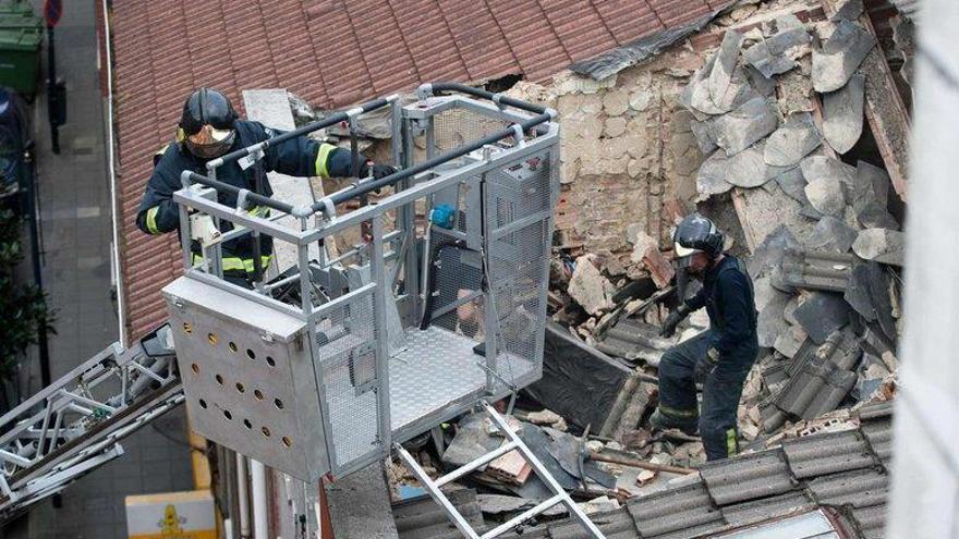 Dos bomberos trabajan en el piso, lleno de escombros tras el derrumbe de la techumbre.