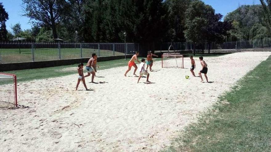 Un grupo de niños juegan al fútbol playa en el arenero de las piscinas.