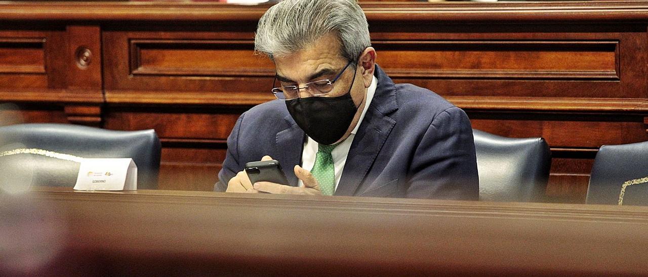 Román Rodríguez, consejero de Hacienda, mira su teléfono móvil durante un pleno del Parlamento de Canarias.