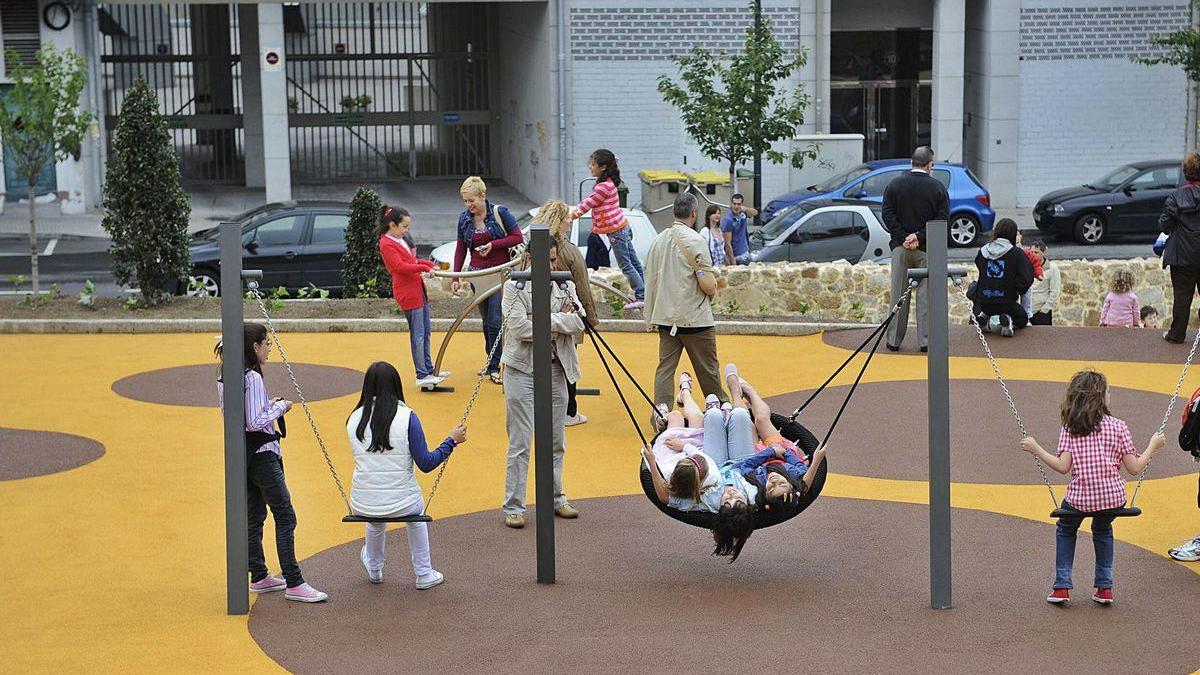 Niños en la zona de juegos infantiles del parque de Oza, acompañados por sus padres.