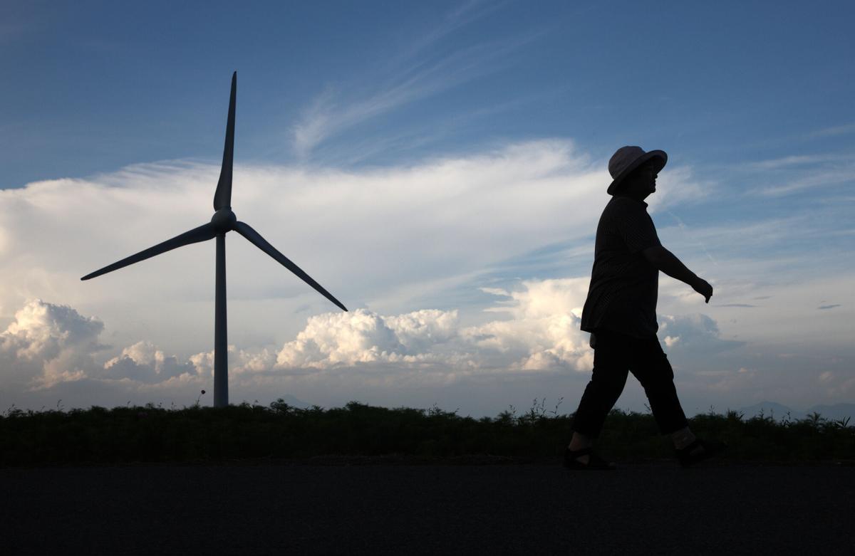 A woman walks past a turbine at the Electric Power Development Co. (J-Power) wind farm in Koriyama City, Fukushima Prefecture, Japan, on Friday, Aug. 24, 2012. Japan's government initiative will require utilities to buy power from renewable energy providers at premium prices under so-called feed-in tariffs. As a result, investment in solar, wind and other forms of clean energy may jump to $17.1 billion from $8.6 billion in 2011, Bloomberg New Energy Finance estimates. Photographer: Tomohiro Ohsumi/Bloomberg. ENERGIA EOLICA