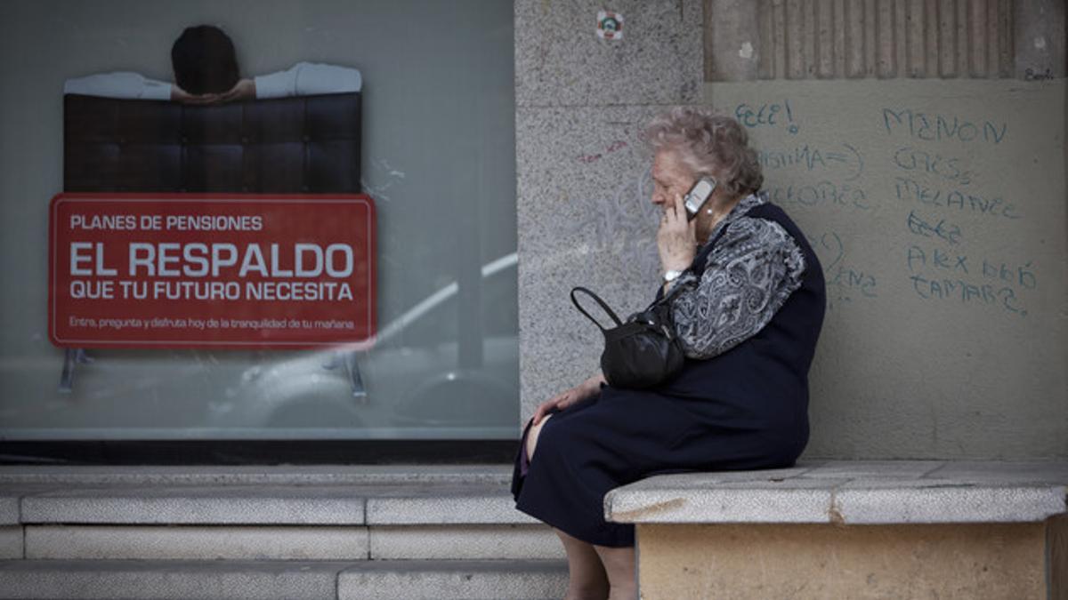 Una mujer mayor habla por teléfono móvil al lado de un cartel de planes de pensiones.