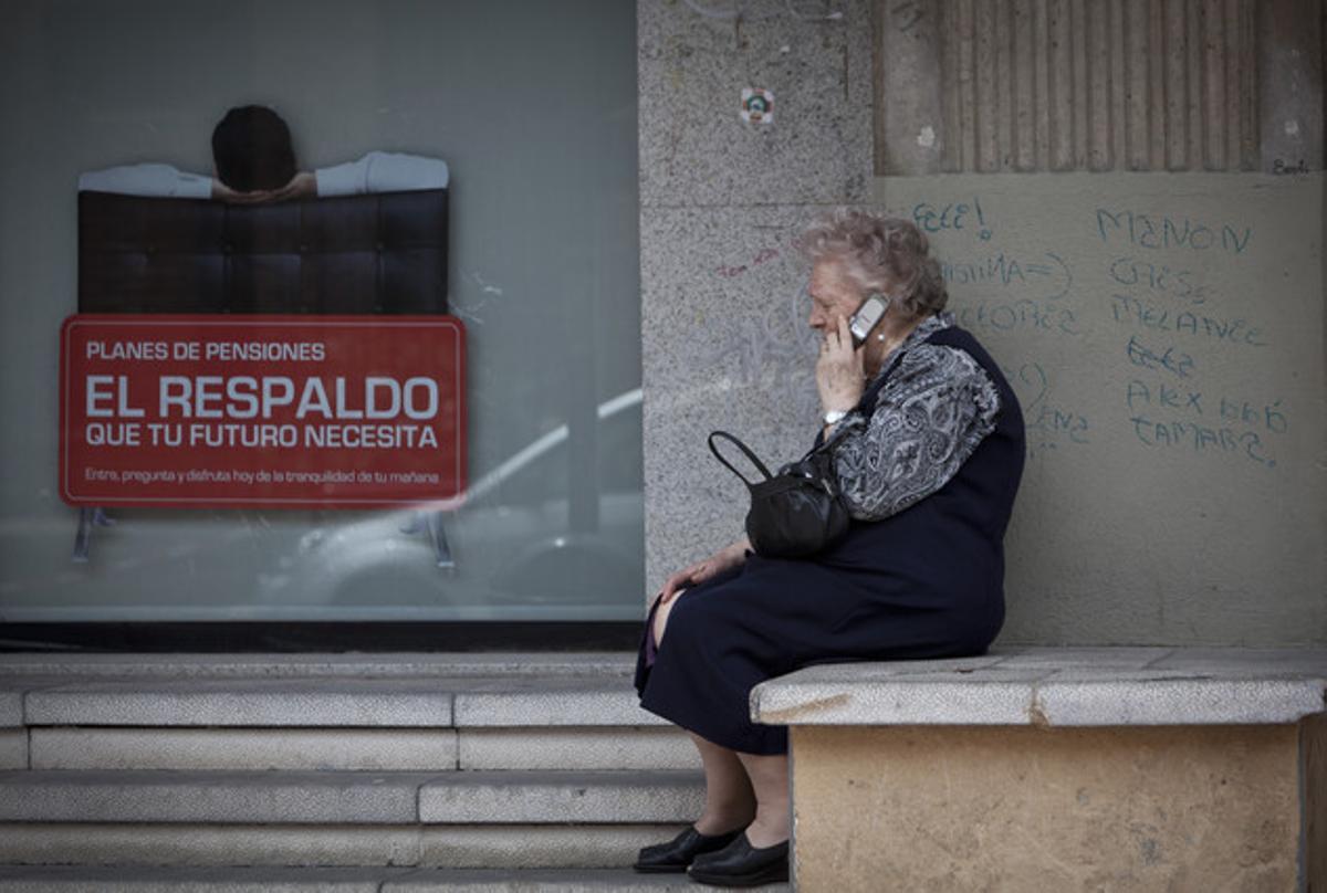 Una dona gran parla per telèfon mòbil al costat d’un cartell de plans de pensions.